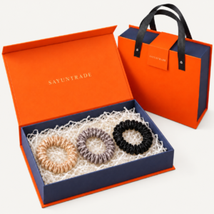 Three slim silk scrunchies presented in an orange and navy gift box with matching gift bag